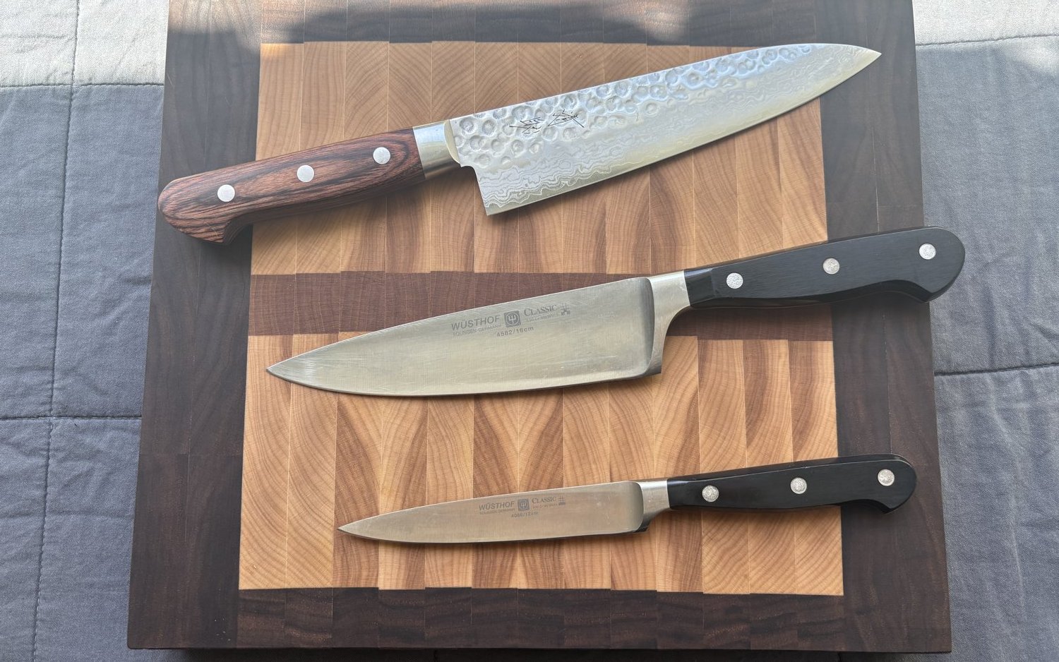 A chef knife, paring knife, and Japanese knife on a walnut cutting board