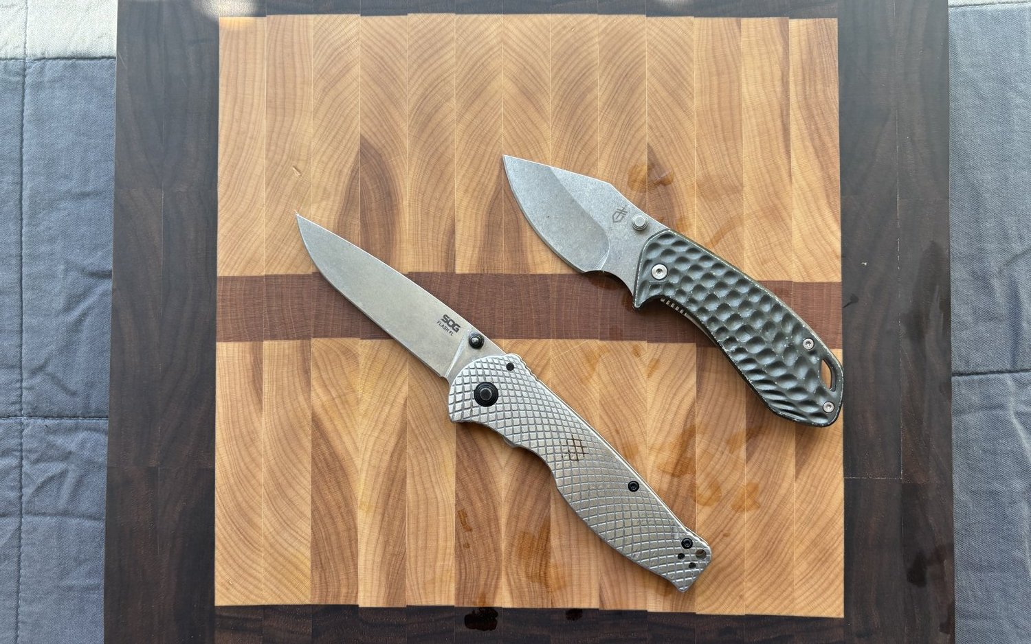 Two folding pocket knives on a walnut cutting board