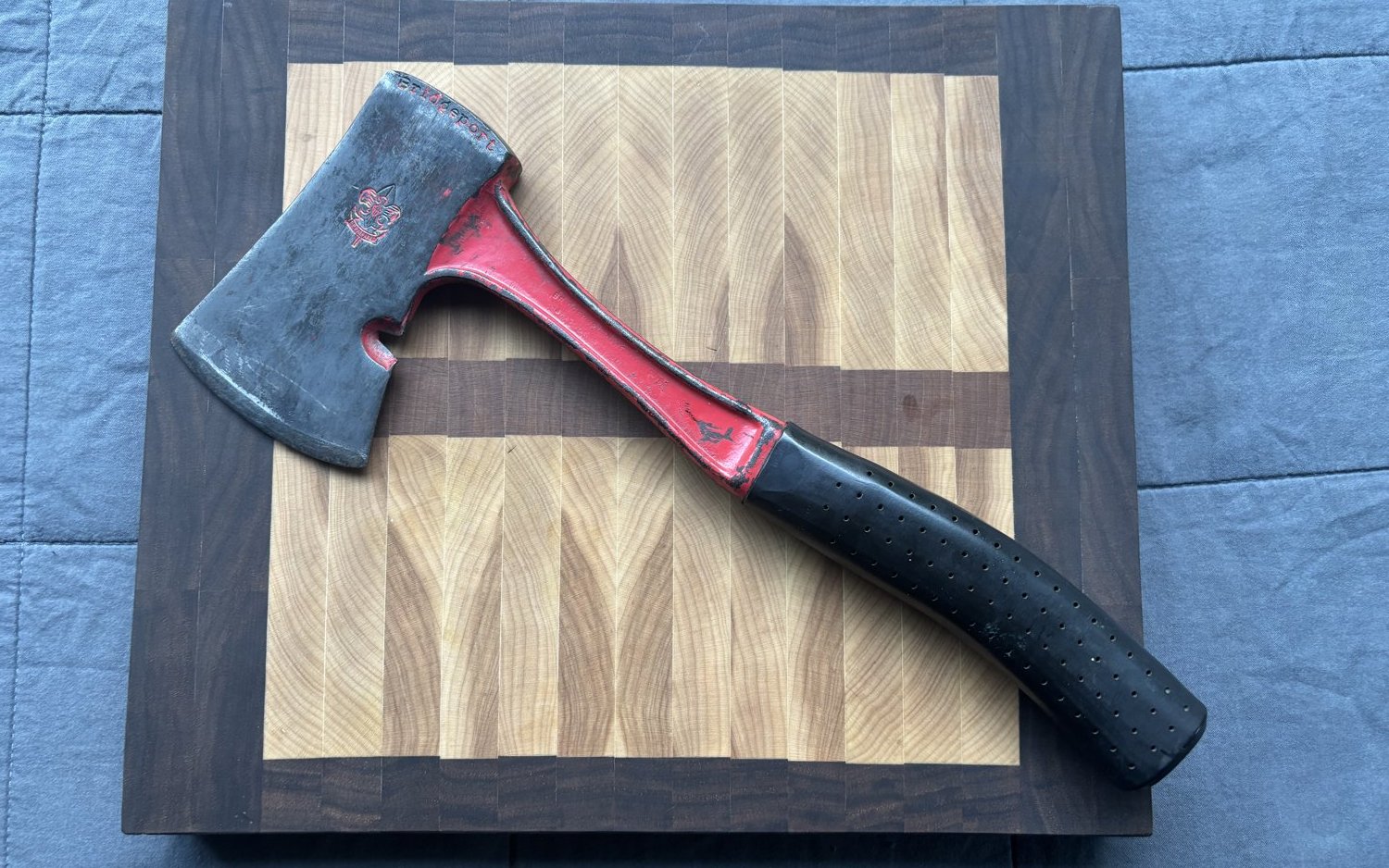 A hatchet with a red head and leather-wrapped handle on a walnut cutting board