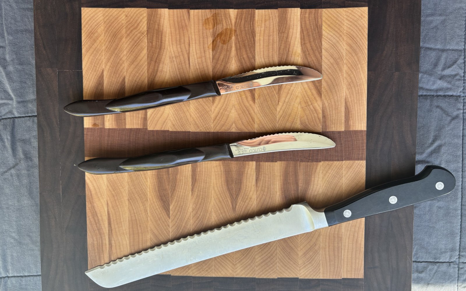A serrated bread knife and two serrated knives on a walnut cutting board